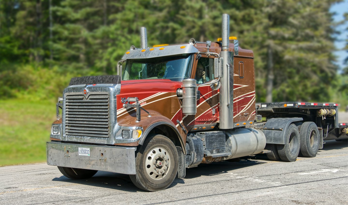 Brown and red semi-truck driving along an asphalt highway.